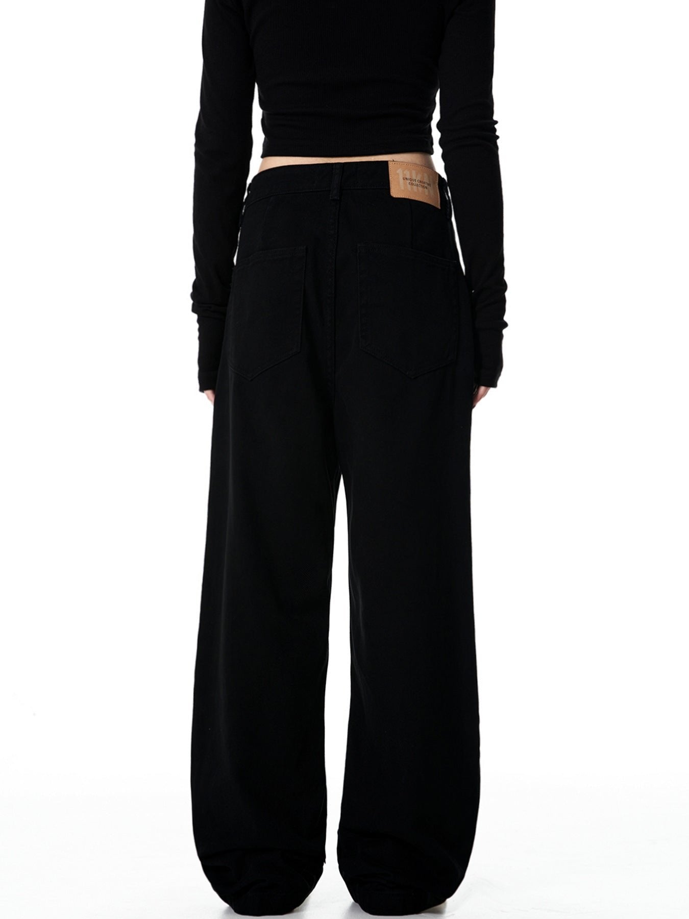 A back view of woman wearing black wide-leg pants showing brand label on waistband, black crop top exposing midriff
