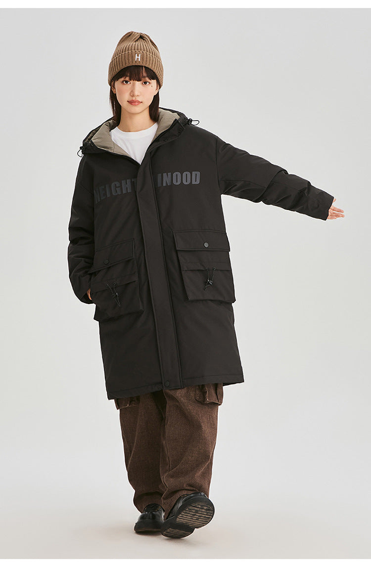 A woman in black NEIGHBORHOOD parka extends arm while wearing brown cord pants and beanie against white background in full-length pose