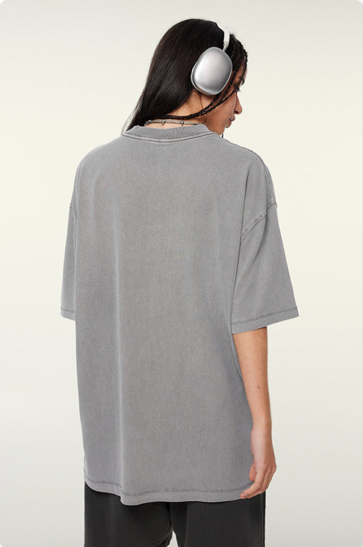 Back view of woman in gray oversized t-shirt with silver headphones showing relaxed fit silhouette