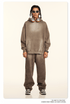 Model with twisted braids wearing taupe sweatsuit set with headphones around neck, standing against cream background