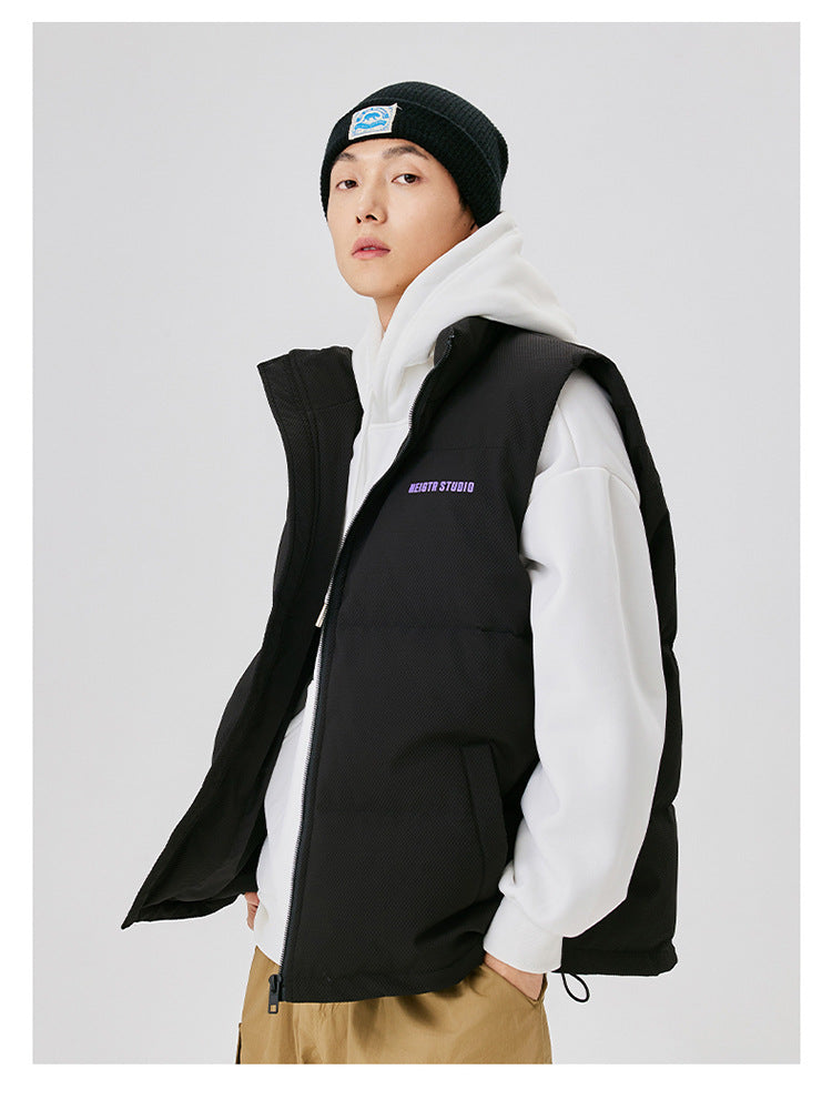 Side view of man wearing black puffer vest with purple NEIGTR STUDIO logo over white hoodie and black beanie against white background