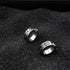 Pair of silver huggie earrings with Roman numeral engravings displayed on black textured background
