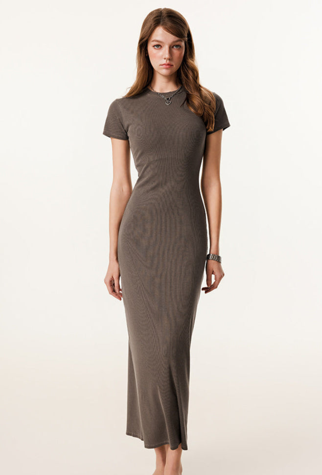 A fashion-forward woman wearing a brown sleeveless maxi dress, paired with tortoiseshell glasses and a plaid handbag.
