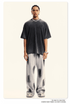 Model with braided hair wearing black oversized t-shirt, silver chain necklace, light gray pants with paint-like markings and white sneakers