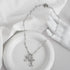 Silver crystal-accented cross pendants on delicate chain necklace displayed on white ceramic dish with mannequin hand