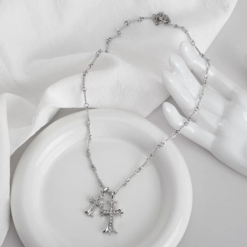 Silver crystal-accented cross pendants on delicate chain necklace displayed on white ceramic dish with mannequin hand