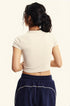 Model stands with her back facing the camera, showcasing the back of a white fitted cropped T-shirt and navy sweat shorts with contrast stitching