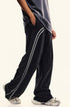 Side view of black washed track pants with gray side stripes, featuring pocket detail and relaxed fit styling with dark top