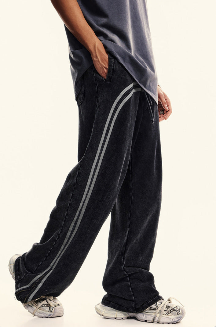 Side view of black washed track pants with gray side stripes, featuring pocket detail and relaxed fit styling with dark top