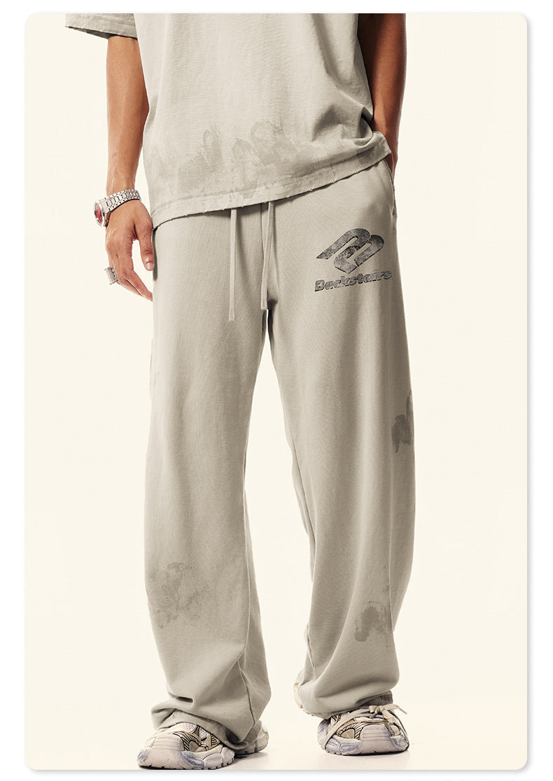 Close-up of model's lower body showing cream Backstairs wide-leg sweatpants with distressed effect, white shoes visible against white background