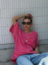 Person wearing a pink shirt and sunglasses sitting against a tiled wall.