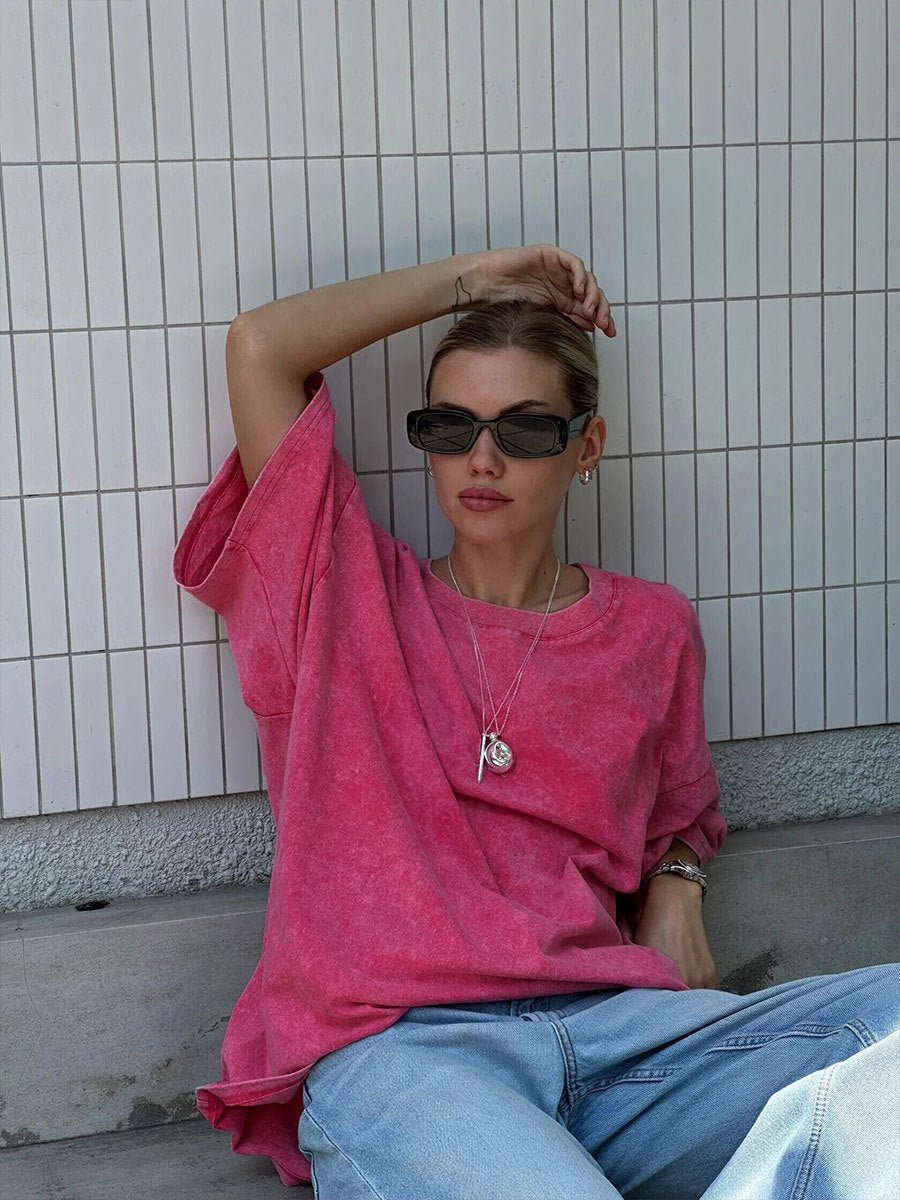 Person wearing a pink shirt and sunglasses sitting against a tiled wall.