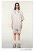 Model with long dark hair wearing oversized light beige t-shirt and matching shorts with white socks and chunky sneakers against neutral background
