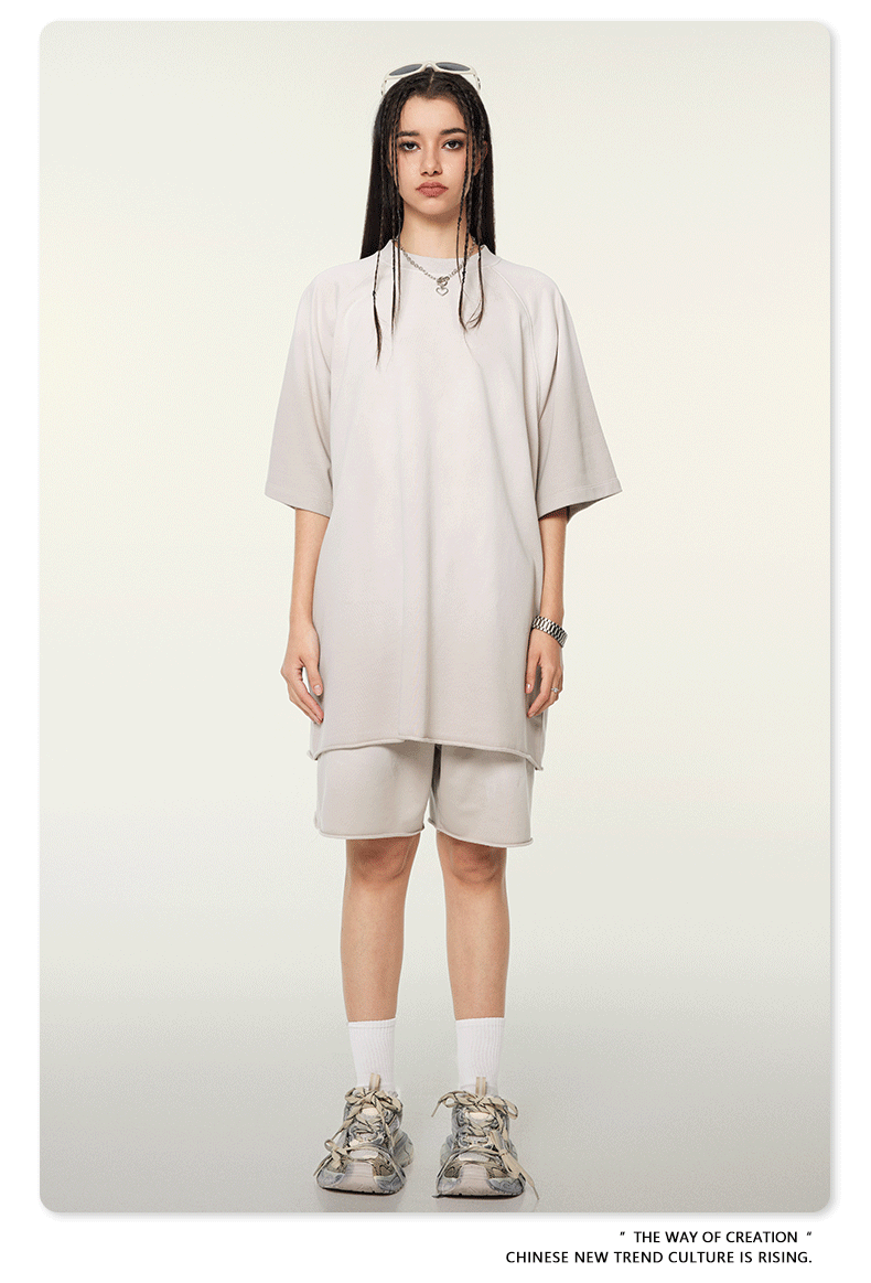 Model with long dark hair wearing oversized light beige t-shirt and matching shorts with white socks and chunky sneakers against neutral background