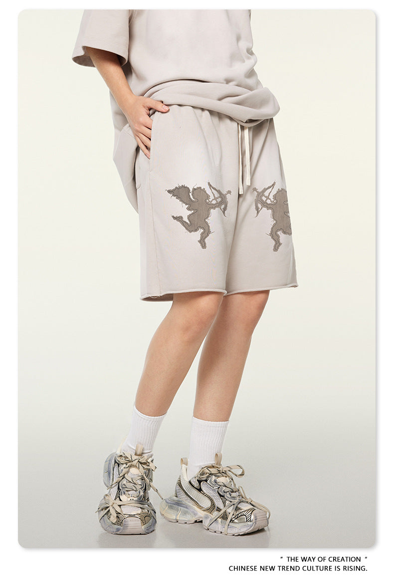 Side profile of beige cotton shorts featuring cupid motifs, styled with oversized matching t-shirt and distressed sneakers