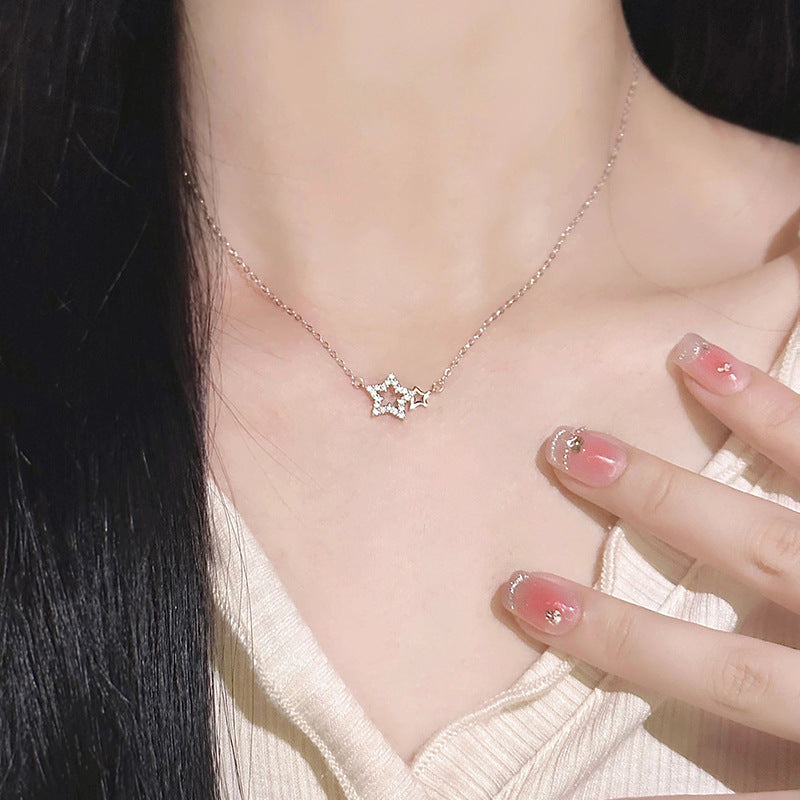 A woman is showcasing a silver crystal-encrusted star pendant necklace while touching her cream top, featuring gradient pink nail art
