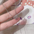 Close-up of silver cat pendant necklace with pink crystal center, held against patterned background
