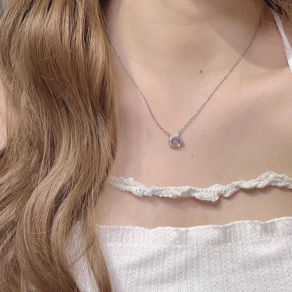 Delicate silver necklace with cat-shaped pendant featuring pink crystal, worn with white lace top