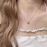 Delicate silver necklace with cat-shaped pendant featuring pink crystal, worn with white lace top