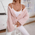 A model is wearing a blush pink cardigan with textured sleeves over white camisole and pants, sitting in a bright room with bookshelf background