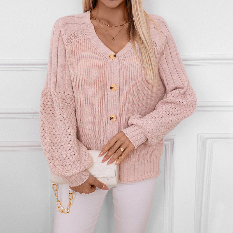 A model is wearing a pink button-up cardigan with puff sleeves holding a white clutch with gold chain, against white paneled wall background