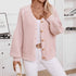 A model is wearing a soft pink cardigan with balloon sleeves over white tank top with gold belt, standing against white bookshelf background