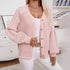 A model is wearing a light pink ribbed cardigan with wooden buttons and textured puff sleeves, paired with white pants and gold accessories