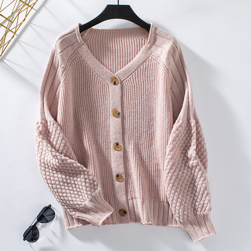 A pink textured cardigan with puff sleeves and wooden buttons displayed on black hanger against white background with sunglasses visible below