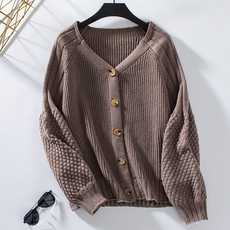 A taupe ribbed cardigan with textured puff sleeves and wooden buttons displayed on hanger against white background with sunglasses below
