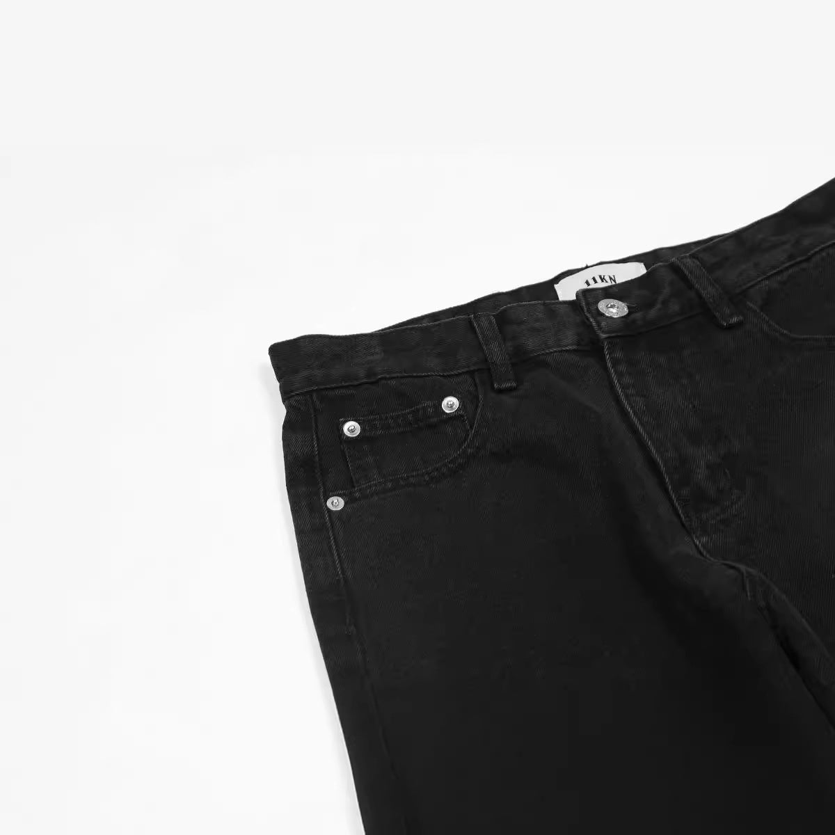 Close-up of black denim jeans pocket detail showing silver rivets and coin pocket construction on white surface