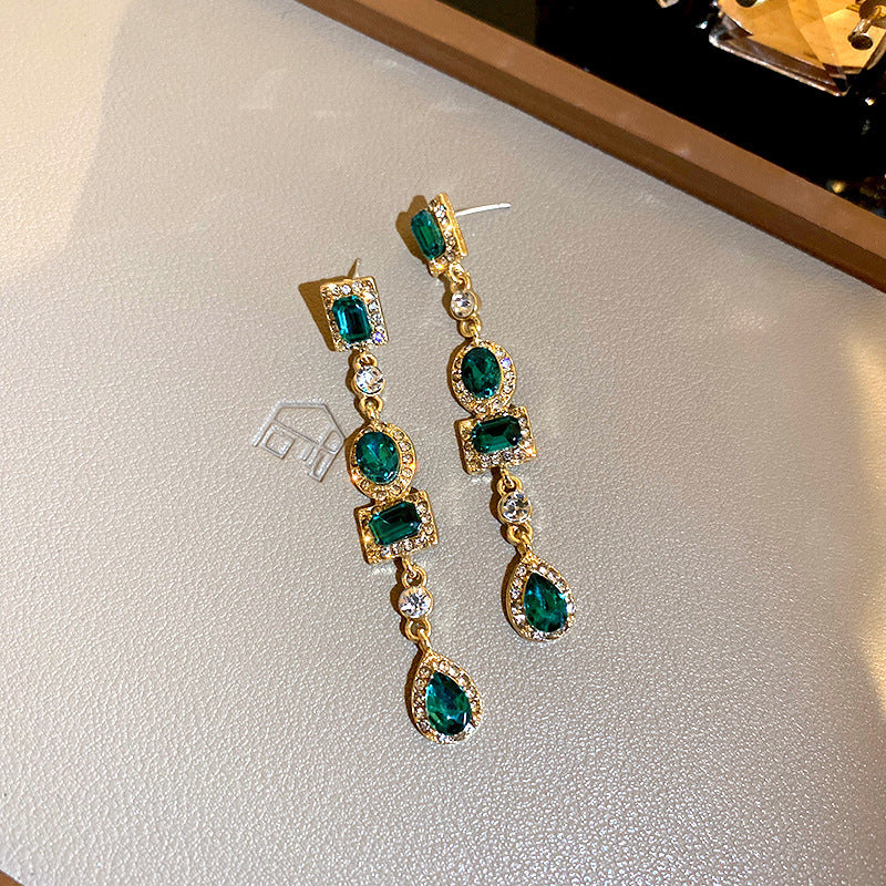 Dangling gold earrings with emerald green rectangular and oval gemstones, adorned with sparkling crystal accents