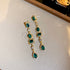 Dangling gold earrings with emerald green rectangular and oval gemstones, adorned with sparkling crystal accents