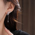 Side profile of silver bow earring with dangling crystal pendant, worn against dark hair with natural lighting