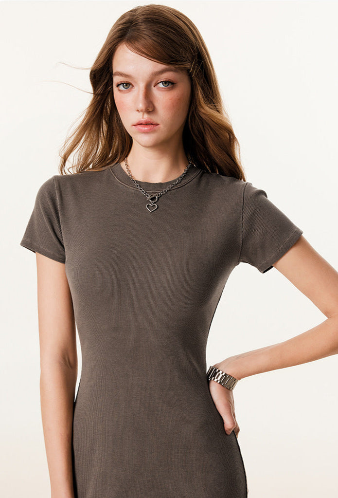 A stylish model in a brown maxi dress, showing details of the ribbed texture and accessorized with a heart pendant necklace.

