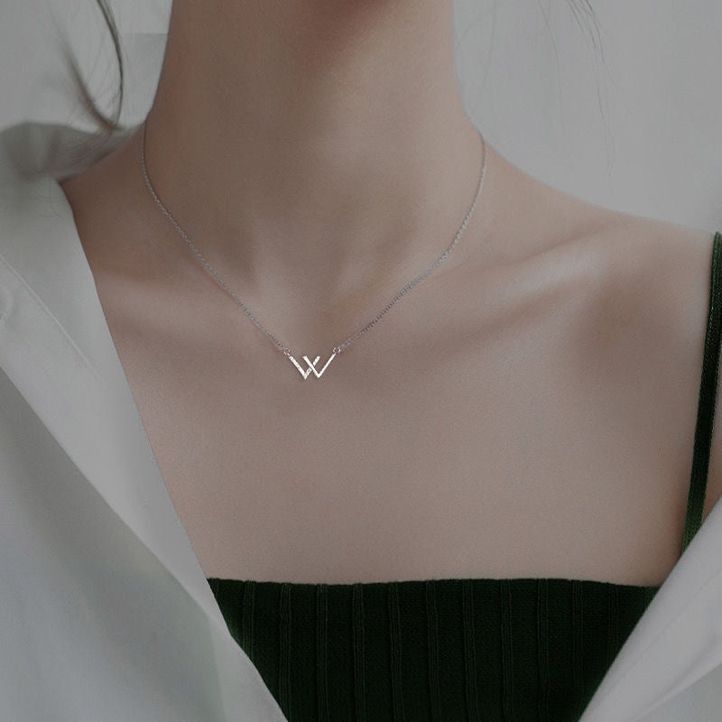 Dainty silver W initial necklace shown on model wearing dark top, demonstrating pendant placement at collarbone