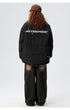 Back view of model showing ASTROSMASH logo across shoulder blades of black puffer jacket with brown wide-leg pants