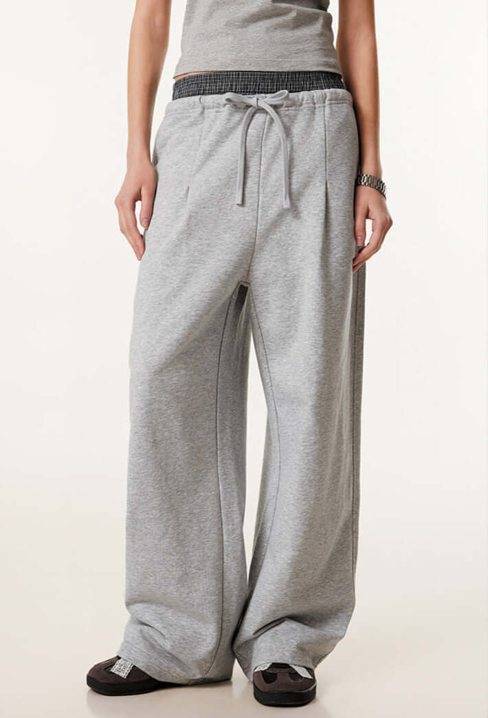 Female model in grey wide-leg sweatpants with a contrast waistband, styled with a grey fitted top and black sneakers.