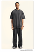 Model wearing charcoal grey oversized t-shirt and relaxed-fit pants with silver chain necklace and watch. Complete monochromatic streetwear look with chunky black shoes