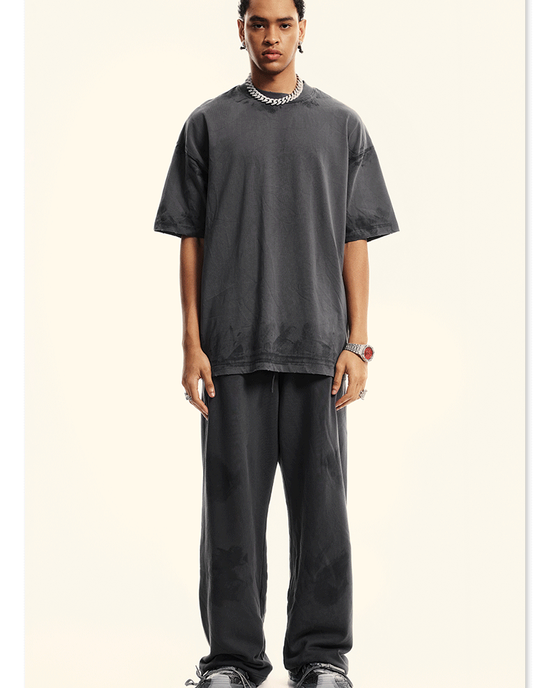 Model wearing charcoal grey oversized t-shirt and relaxed-fit pants with silver chain necklace and watch. Complete monochromatic streetwear look with chunky black shoes