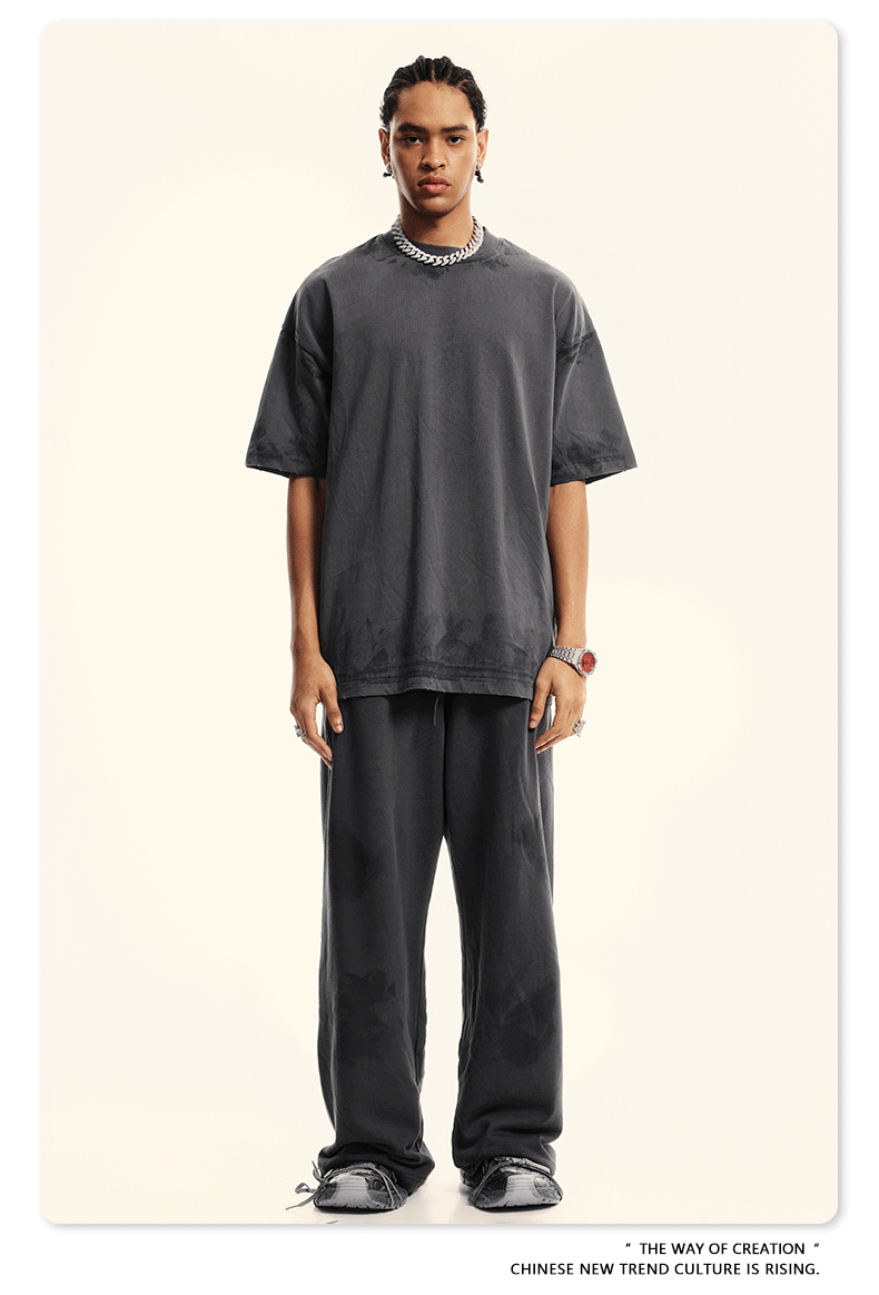 Model wearing charcoal grey oversized t-shirt and relaxed-fit pants with silver chain necklace and watch. Complete monochromatic streetwear look with chunky black shoes