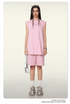 Model wearing light pink matching set with oversized sleeveless top and shorts, white sneakers, silver chain necklace and sunglasses on head on neutral background