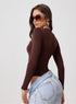 Woman wearing a brown long-sleeve top and light blue jeans on a plain background