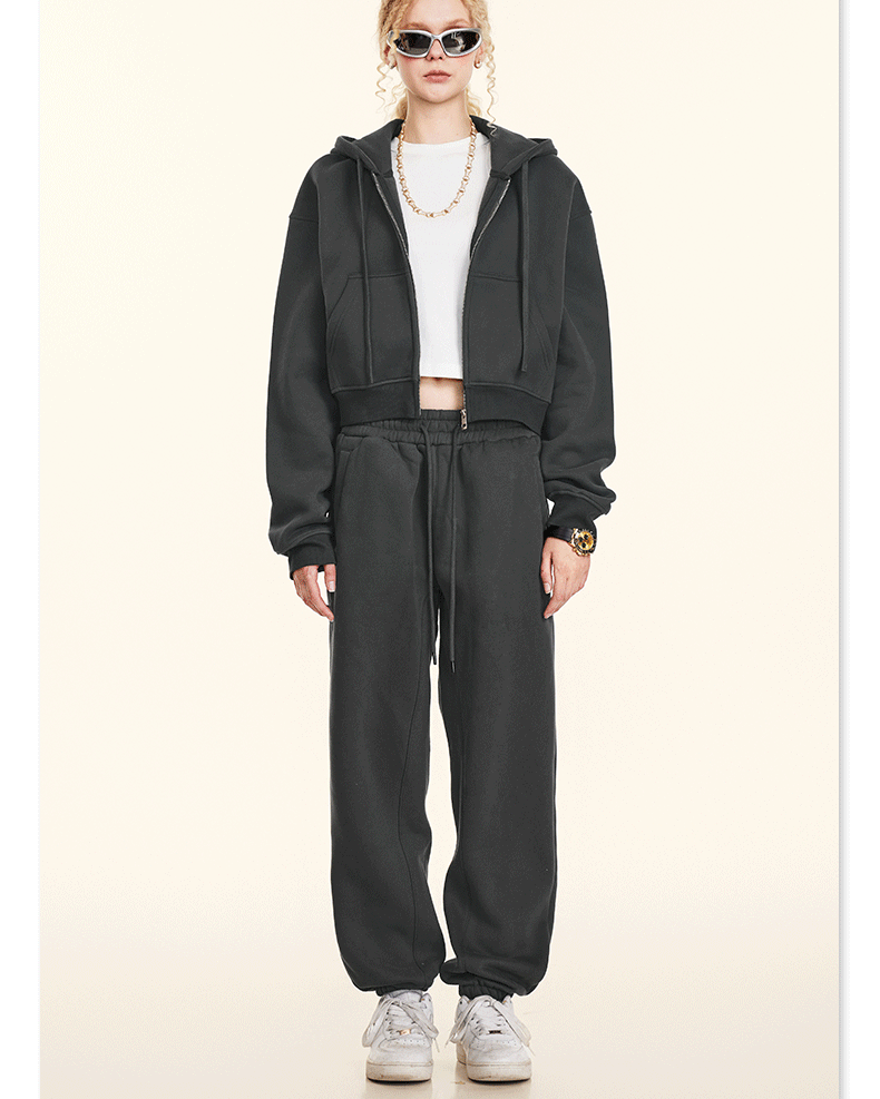 Model posing in black athleisure set with cropped hoodie and joggers. Paired with white sneakers and sunglasses