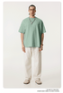 Model in mint green oversized t-shirt paired with cream wide-leg pants and beige slip-on shoes, featuring silver chain necklace with white pendant