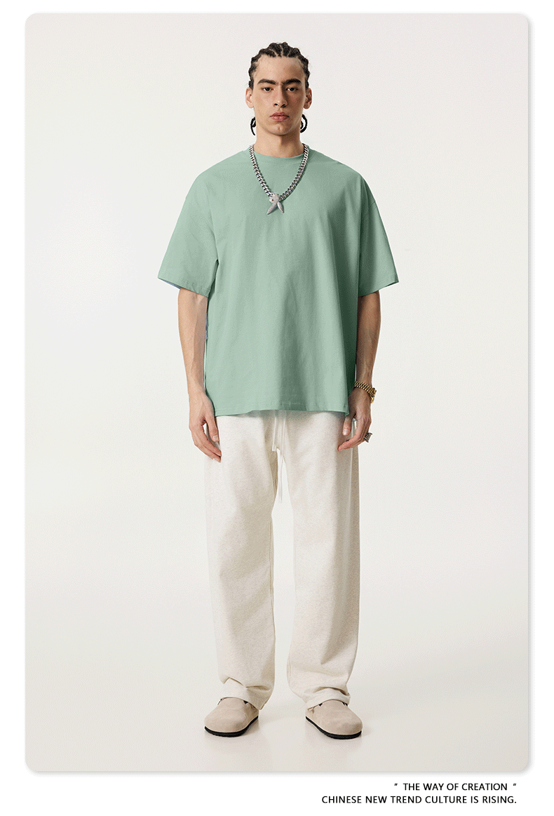 Model in mint green oversized t-shirt paired with cream wide-leg pants and beige slip-on shoes, featuring silver chain necklace with white pendant