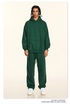 Model wearing forest green hoodie and sweatpants with white sneakers and silver accessories