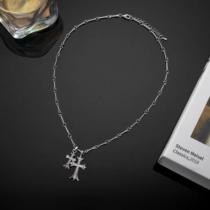 Silver chain necklace with ornate crystal cross pendant displayed on black surface next to drinking glass and book
