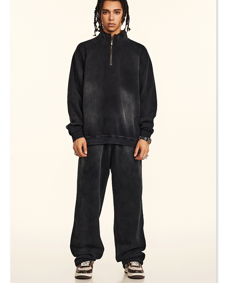 Model with twisted hair wearing black half-zip pullover and wide-leg sweatpants, square sunglasses, sneakers, cream backdrop