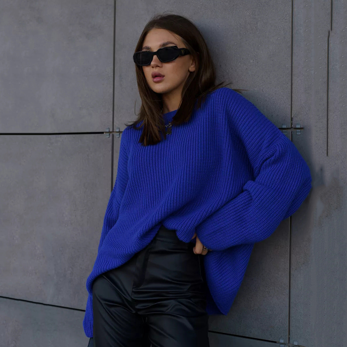 Woman in bright royal blue oversized sweater with sunglasses against industrial background