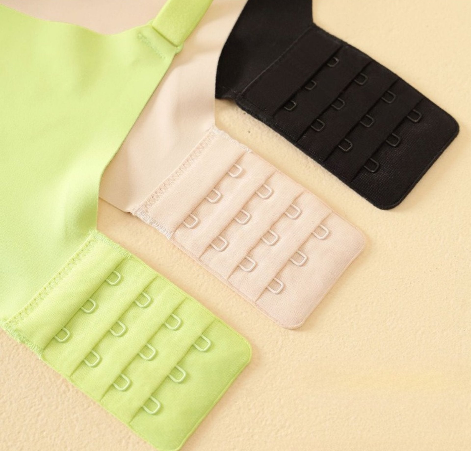 Light green, beige, and black bras with four-row hook closures for fit adjustment.
